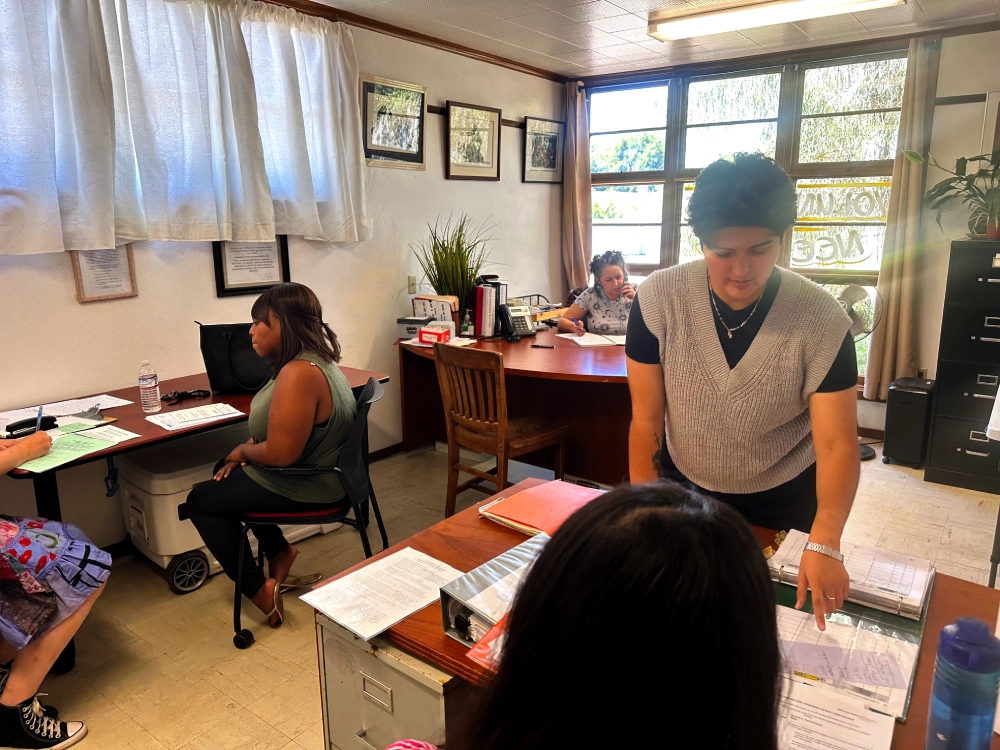 Volunteers in an office transacting, talking on the phone and one woman pointing to a binder