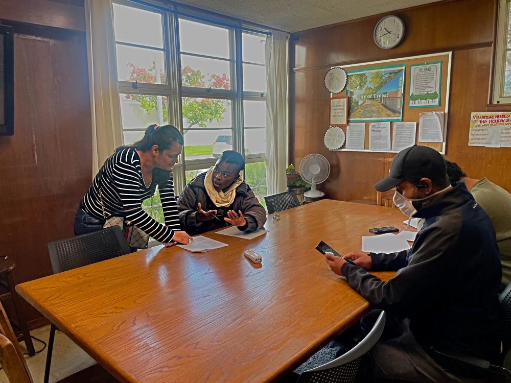 Four people in an office. One woman explaining to another woman paperwork while two men sit across from them.