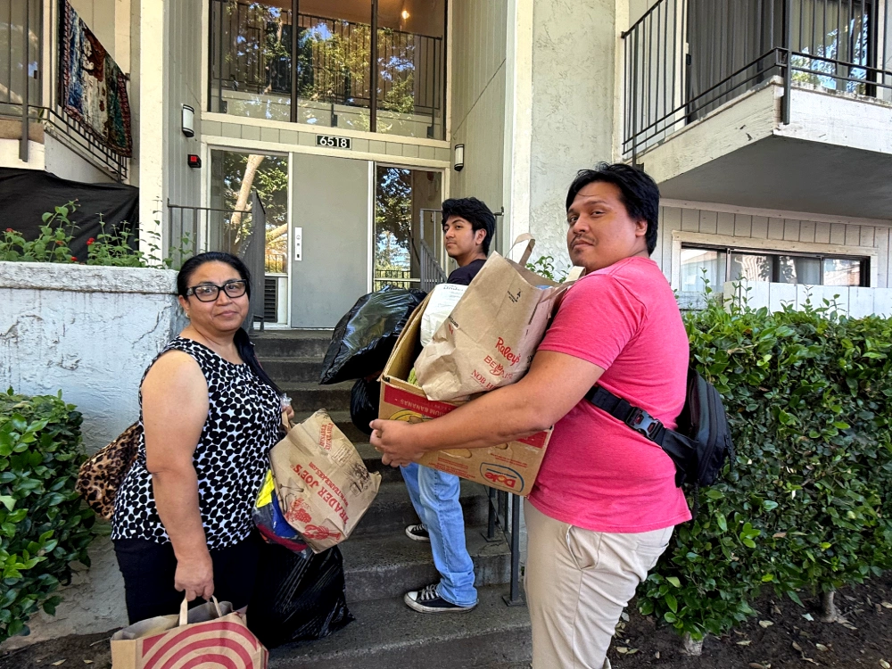 Two men help woman bring bags and boxes up a flight of stairs
