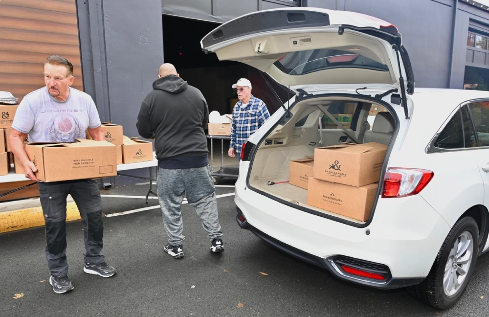 Three men load boxes in the trunk of a car.