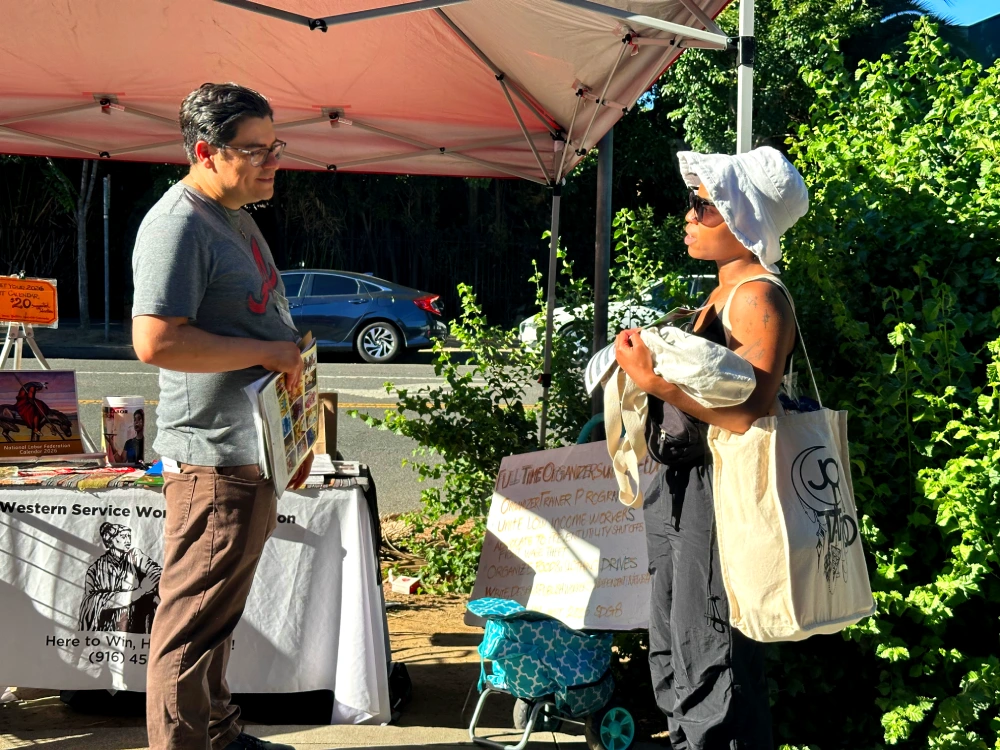 Man listens to woman speaking under a red pop-up tent.
