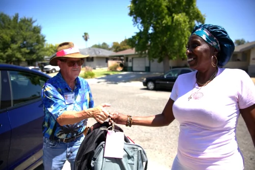 Man in blue hands backpacks to woman smiling.