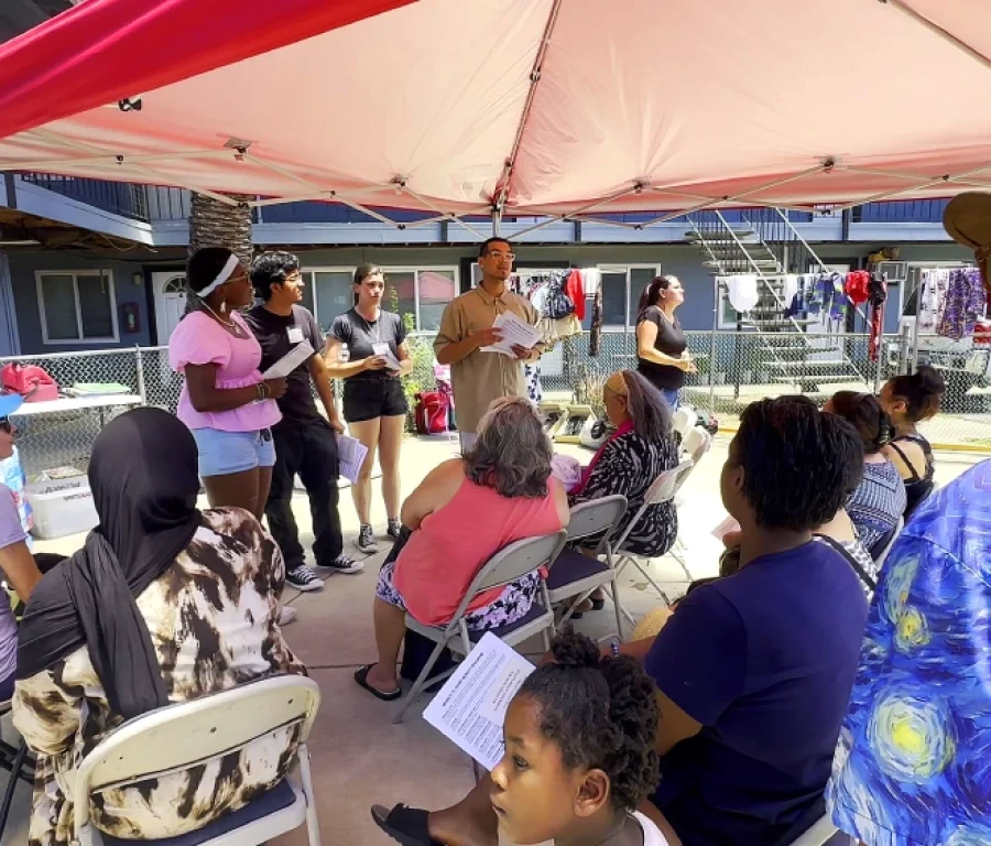 Volunteers give a presentation under a tent with residents seated in folding chairs